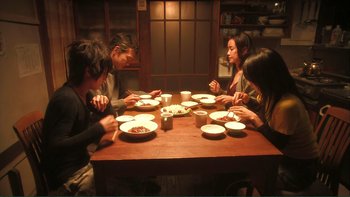 Movie still from “Love Exposure” (2008), directed by Sion Sono – A group of people sitting at a table with plates of food; Wide shot, High angle