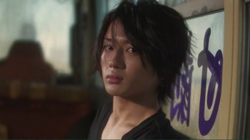 Movie still from “Love Exposure” (2008), directed by Sion Sono – A young man with long black hair is looking at the camera; Close Up shot, Low angle