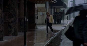 Movie still from “Love Liza” (2002), directed by Todd Louiso – A woman walking down the sidewalk in the rain; Wide shot, High angle