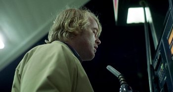 Movie still from “Love Liza” (2002), directed by Todd Louiso – A man with blonde hair is speaking into a microphone; Close Up shot, Low angle
