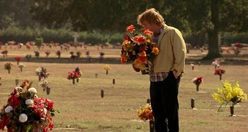 Movie still from “Love Liza” (2002), directed by Todd Louiso – A man holding a bouquet of flowers in a cemetery; Wide shot, Over the shoulder angle