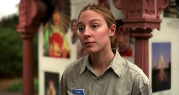 Movie still from “Love Liza” (2002), directed by Todd Louiso – A woman with a name tag in front of a wall of pictures; Close Up shot, Over the shoulder angle