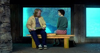 Movie still from “Love Liza” (2002), directed by Todd Louiso – A man and a woman sitting on a bench in front of an aquarium; Medium shot, Over the shoulder angle