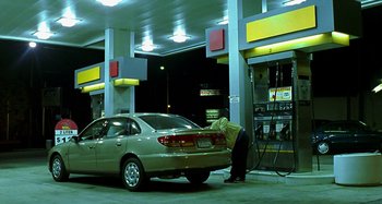 Movie still from “Love Liza” (2002), directed by Todd Louiso – A person filling up a car at a gas station at night; Wide shot, High angle