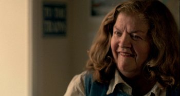 Movie still from “Love Liza” (2002), directed by Todd Louiso – An older woman with long brown hair is smiling for the camera; Close Up shot, Over the shoulder angle