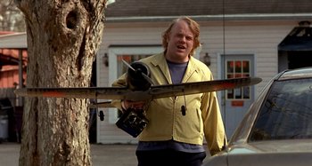 Movie still from “Love Liza” (2002), directed by Todd Louiso – A man in a yellow jacket holding a wooden plane; Medium shot, Low angle