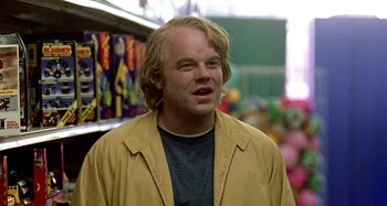 Movie still from “Love Liza” (2002), directed by Todd Louiso – A man with blonde hair and a blue t - shirt is standing in a store; Close Up shot, Over the shoulder angle