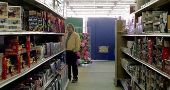 Movie still from “Love Liza” (2002), directed by Todd Louiso – A man standing inside of a store looking at balloons; Wide shot, Over the shoulder angle