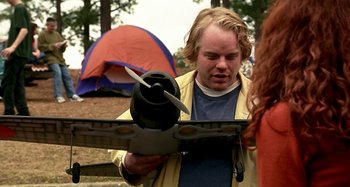 Movie still from “Love Liza” (2002), directed by Todd Louiso – A young man holding an object in front of a tent; Medium shot, Over the shoulder angle