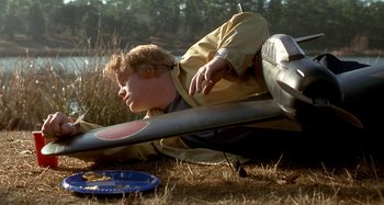 Movie still from “Love Liza” (2002), directed by Todd Louiso – A young boy laying on the ground next to an airplane; Medium shot, High angle