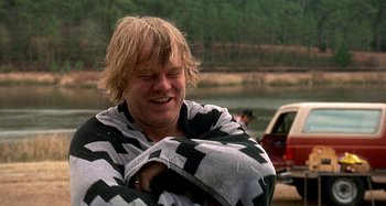 Movie still from “Love Liza” (2002), directed by Todd Louiso – A man wrapped in a blanket near a body of water; Medium shot, Over the shoulder angle