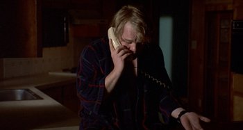 Movie still from “Love Liza” (2002), directed by Todd Louiso – A man talking on a phone while sitting in a chair; Medium shot, High angle
