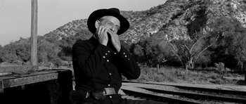 Movie still from “Love Me Tender” (1956), directed by Robert D. Webb – An older man in a black hat and a black shirt is sitting on a rail road track; Medium shot, Low angle