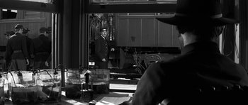 Movie still from “Love Me Tender” (1956), directed by Robert D. Webb – A black and white photo of a man in a train station; Medium shot, Over the shoulder angle