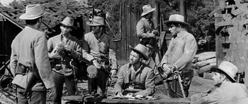 Movie still from “Love Me Tender” (1956), directed by Robert D. Webb – A black and white photo of a group of men sitting on a bench; Medium shot, Low angle