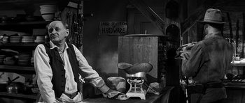 Movie still from “Love Me Tender” (1956), directed by Robert D. Webb – A man sitting on top of a table next to a pair of shoes; Medium shot, Low angle