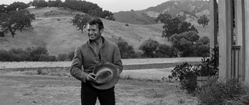 Movie still from “Love Me Tender” (1956), directed by Robert D. Webb – A black and white photo of a man holding a cowboy hat; Medium shot, Low angle