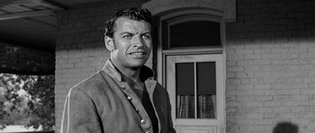 Movie still from “Love Me Tender” (1956), directed by Robert D. Webb – Black and white photograph of a man in front of a building; Close Up shot, Low angle