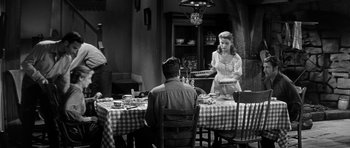 Movie still from “Love Me Tender” (1956), directed by Robert D. Webb – A black - and - white photo of a man and a woman sitting at a dinner table; Medium shot, High angle