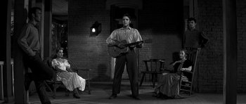 Movie still from “Love Me Tender” (1956), directed by Robert D. Webb – A man holding a guitar while standing next to a woman; Wide shot, Low angle