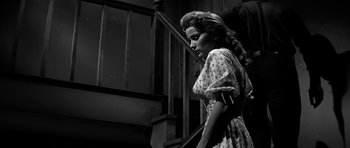 Movie still from “Love Me Tender” (1956), directed by Robert D. Webb – A woman in a dress standing next to a staircase; Medium shot, Low angle