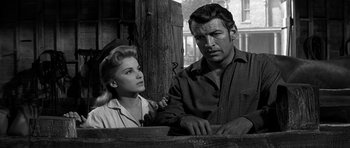 Movie still from “Love Me Tender” (1956), directed by Robert D. Webb – A man and a woman standing next to each other in front of a wooden pole; Medium shot, Low angle