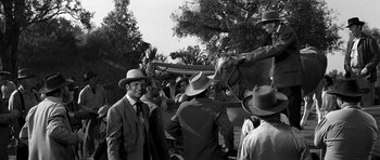 Movie still from “Love Me Tender” (1956), directed by Robert D. Webb – A black and white photo of a group of men standing next to a horse; Wide shot, Over the shoulder angle