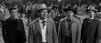 Movie still from “Love Me Tender” (1956), directed by Robert D. Webb – A black and white photo of two men in suits and hats in front of a crowd; Medium shot, Over the shoulder angle