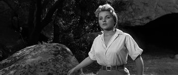 Movie still from “Love Me Tender” (1956), directed by Robert D. Webb – A black - and - white photo of a woman standing next to a rock; Medium shot, Low angle
