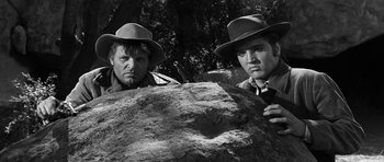 Movie still from “Love Me Tender” (1956), directed by Robert D. Webb – A couple of men standing next to each other on top of a rock; Medium shot, Low angle