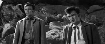 Movie still from “Love Me Tender” (1956), directed by Robert D. Webb – Two men standing next to each other near a rocky area; Medium shot, Over the shoulder angle