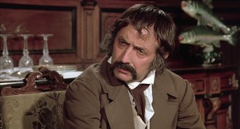 Movie still from “Love and Death” (1975), directed by Woody Allen – A man with a beard and mustache sitting in a room; Close Up shot, Over the shoulder angle