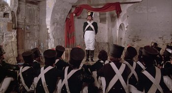 Movie still from “Love and Death” (1975), directed by Woody Allen – A group of men dressed in uniforms are sitting in front of a man in a uniform; Wide shot, High angle