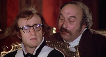 Movie still from “Love and Death” (1975), directed by Woody Allen – A man and a woman sitting next to each other in a room; Close Up shot, Over the shoulder angle