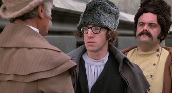 Movie still from “Love and Death” (1975), directed by Woody Allen – A man wearing a fur hat and glasses is standing next to another man; Close Up shot, Over the shoulder angle
