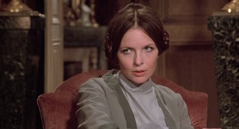 Movie still from “Love and Death” (1975), directed by Woody Allen – A woman sitting in a chair wearing a gray jacket; Close Up shot, Over the shoulder angle