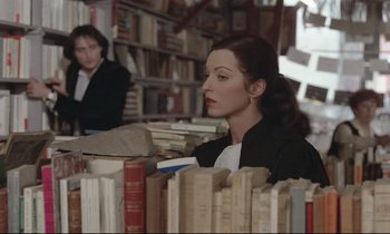 Movie still from “Love on the Run” (1979), directed by François Truffaut – A woman sitting in front of a book shelf; Medium shot, High angle