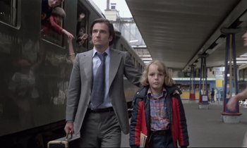 Movie still from “Love on the Run” (1979), directed by François Truffaut – A man and a boy are walking on a train platform; Medium shot, Low angle