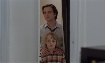 Movie still from “Love on the Run” (1979), directed by François Truffaut – A man standing next to a young boy in front of a door; Medium shot, Low angle