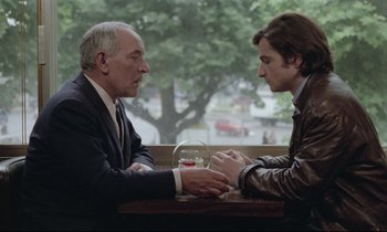 Movie still from “Love on the Run” (1979), directed by François Truffaut – Two men sitting at a table with a glass of red wine; Medium shot, Over the shoulder angle