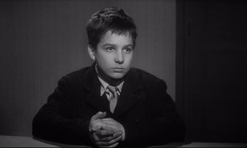 Movie still from “Love on the Run” (1979), directed by François Truffaut – A young man in a suit and tie sitting in front of a wall; Medium shot, High angle