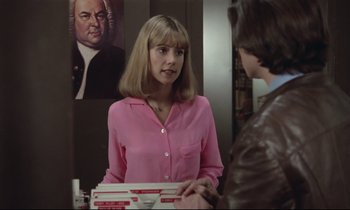 Movie still from “Love on the Run” (1979), directed by François Truffaut – A woman in a pink shirt is holding a stack of pizza; Medium shot, Over the shoulder angle