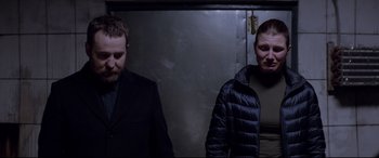 Movie still from “Loveless” (2017), directed by Andrey Zvyagintsev – Two men standing next to each other in front of a metal wall; Medium shot, Over the shoulder angle