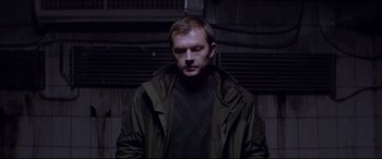 Movie still from “Loveless” (2017), directed by Andrey Zvyagintsev – A man in a green jacket standing in a dark room; Medium shot, Low angle