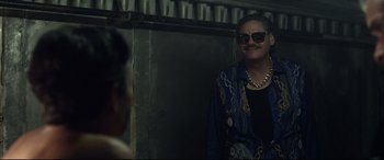 A woman wearing sunglasses standing next to a wall