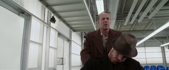 Movie still from “Lucky Number Slevin” (2006), directed by Paul McGuigan – A man sitting on top of a chair next to another man; Medium shot, Low angle