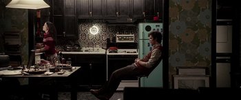 Movie still from “Lucky Number Slevin” (2006), directed by Paul McGuigan – A man sitting on a chair in a kitchen next to a refrigerator; Wide shot, High angle