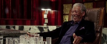 Movie still from “Lucky Number Slevin” (2006), directed by Paul McGuigan – An older man sitting in a chair in front of a table; Close Up shot, Over the shoulder angle