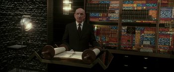 Movie still from “Lucky Number Slevin” (2006), directed by Paul McGuigan – A man in a suit and tie sitting in front of a table; Medium shot, Low angle