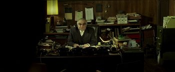 Movie still from “Lucky Number Slevin” (2006), directed by Paul McGuigan – An older man sitting at a desk in front of a computer; Wide shot, High angle